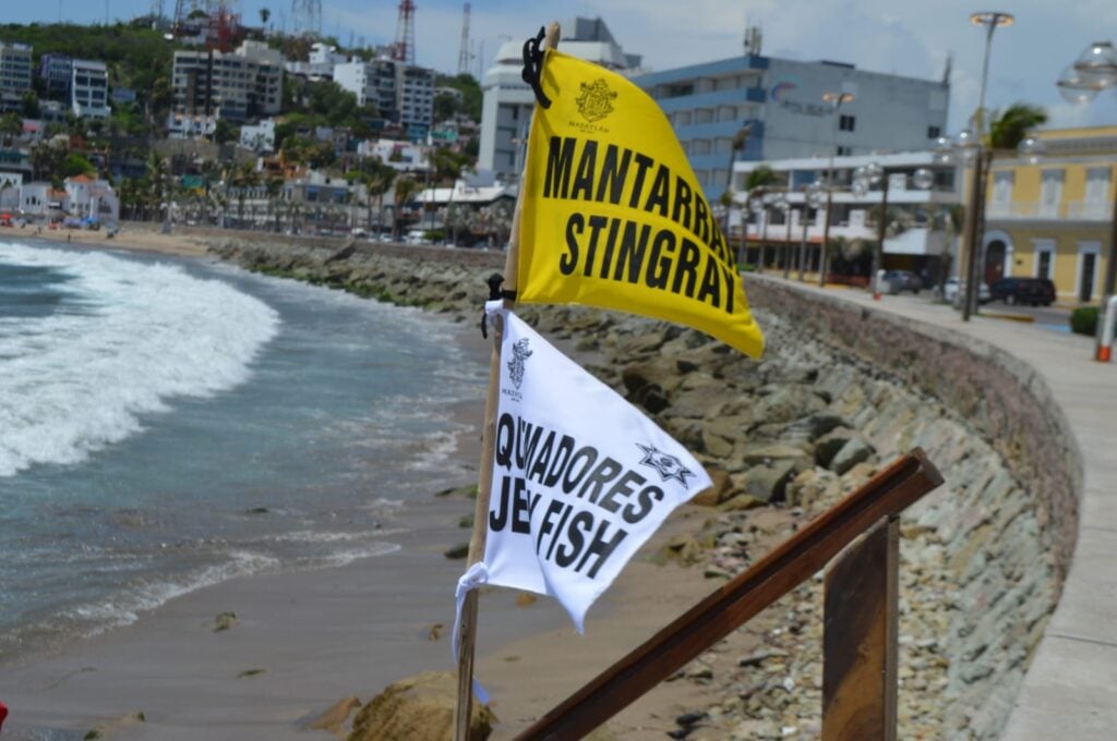 2 banderas una amarilla y una blanca de mantarrayas y quemadores en la playa de Mazatlán