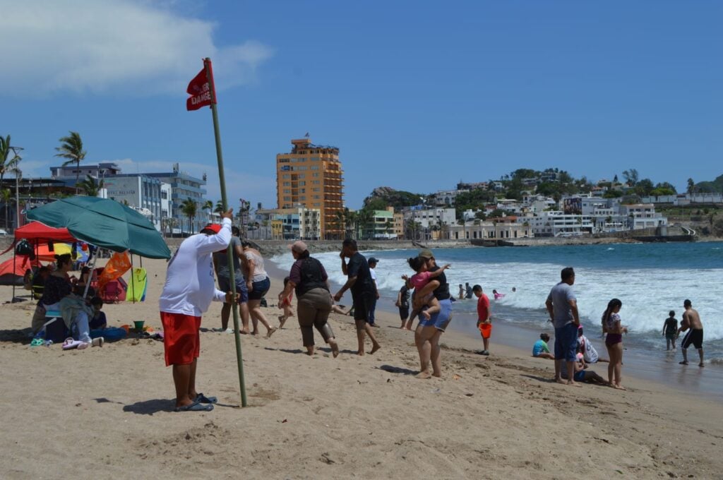 Una persona poniendo la bandera roja de peligro en la orilla de la playa en Mazatlán y más personas