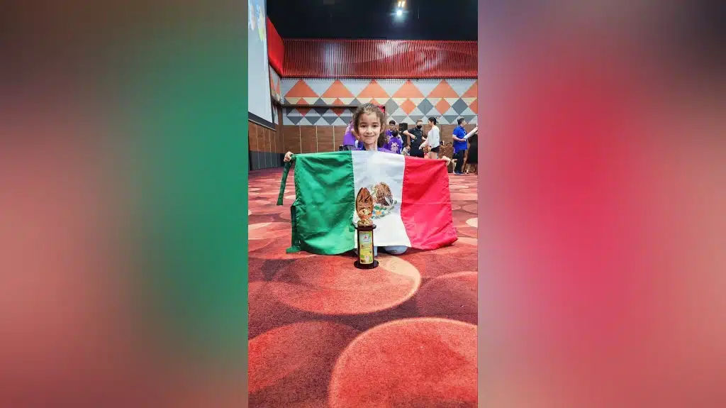La pequeña Regina Rass posa con la bandera de México y el trofeo del Campeonato Mundial de Cálculo Aloha 2023