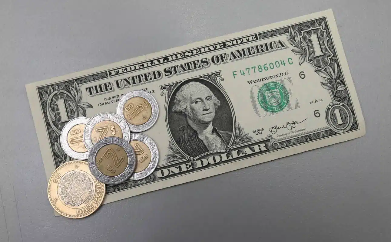 Un billete de dólar y monedas mexicanas sobre él