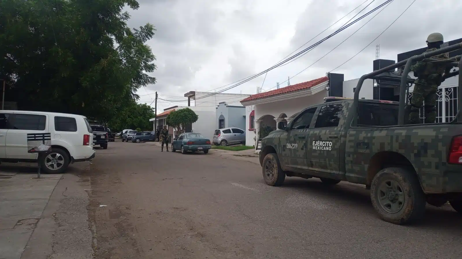 Camión, camioneta y personas con uniforme del Ejército Mexicano, casas y carros estacionados