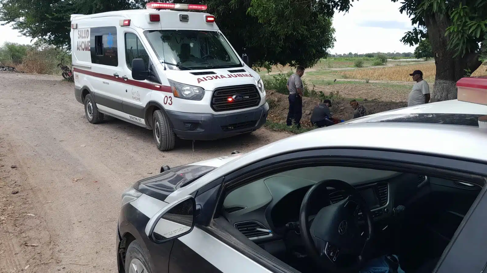 En primer plano una patrulla de la Policía Municipal, de fondo una ambulancia de SUMMA en campos de cultivo de Ahome