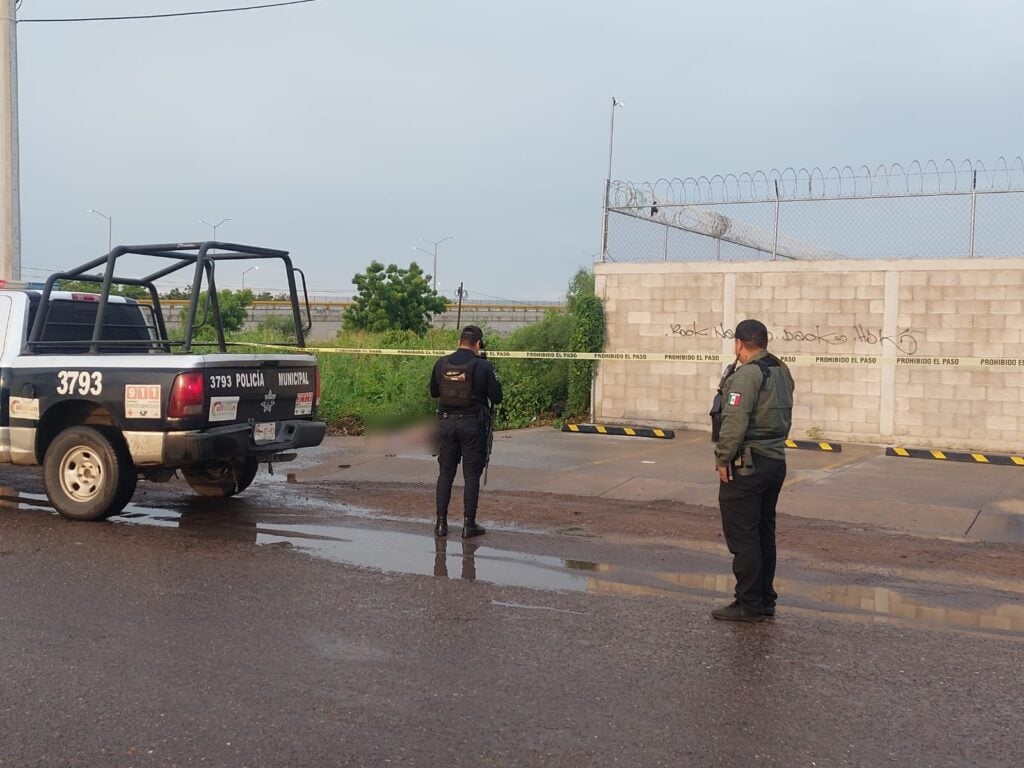 Una camioneta de la policía municipal, 2 personas y cinta amarilla delimitando el área de un crimen