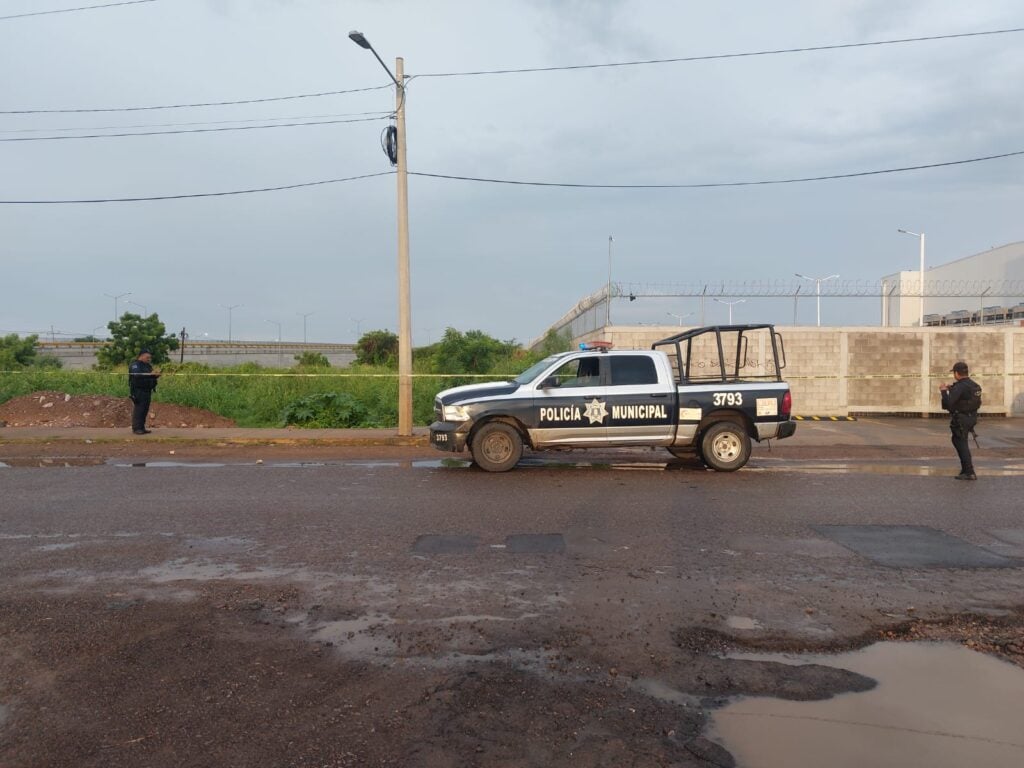 Una camioneta de la policía municipal, 2 personas y cinta amarilla delimitando el área de un crimen