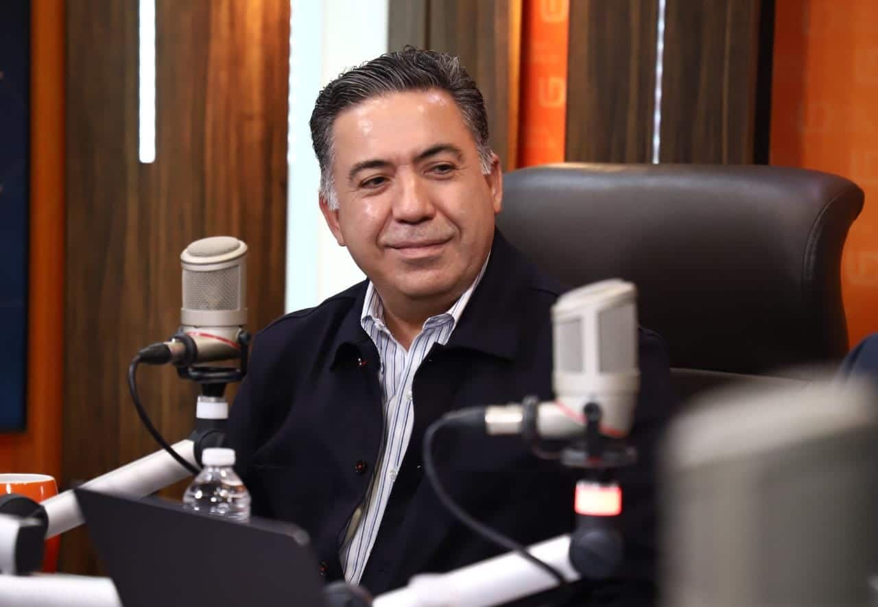 Una persona sentada sonriendo y micrófonos de un estudio de radio