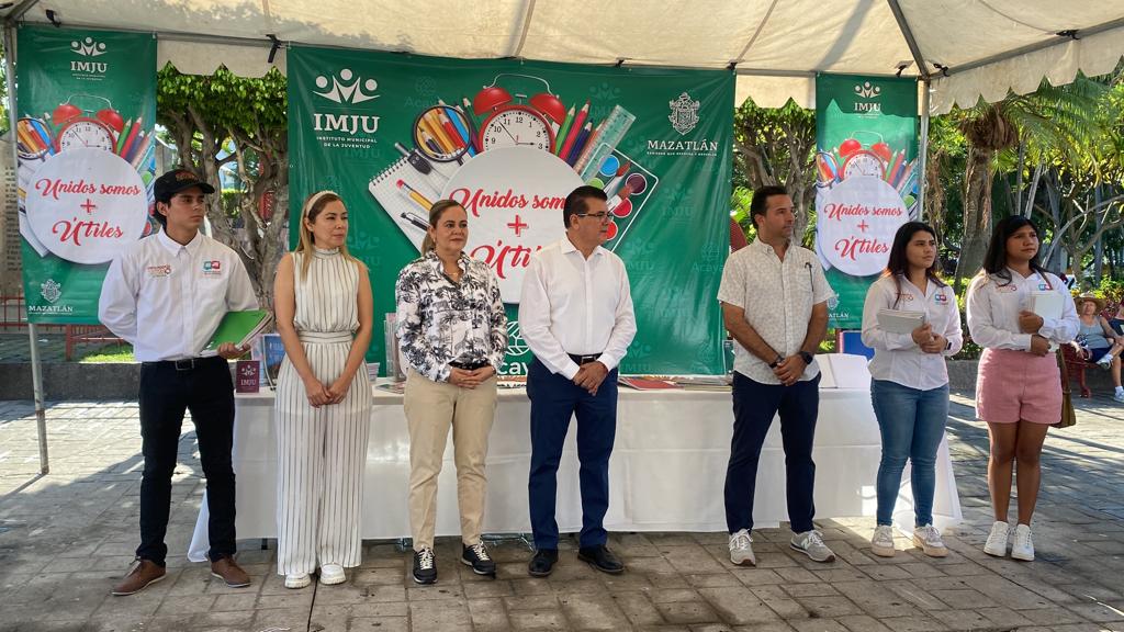 7 personas paradas y al fondo una lona con letras y logotipos