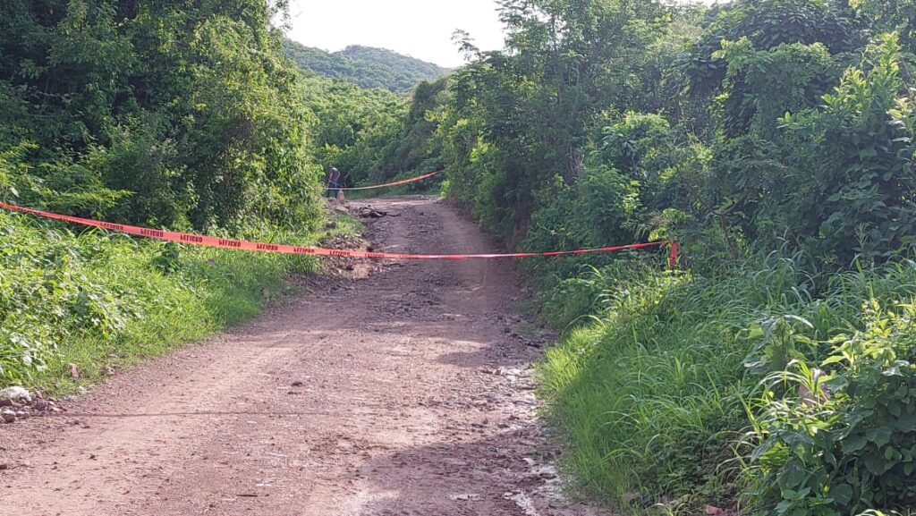 Camino de terracería acordonado con cinta roja tras localizar a un hombre asesinado