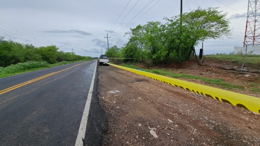 Cinta amarilla delimitando la escena de un crimen, árboles, carretera y una camioneta de la Semefo