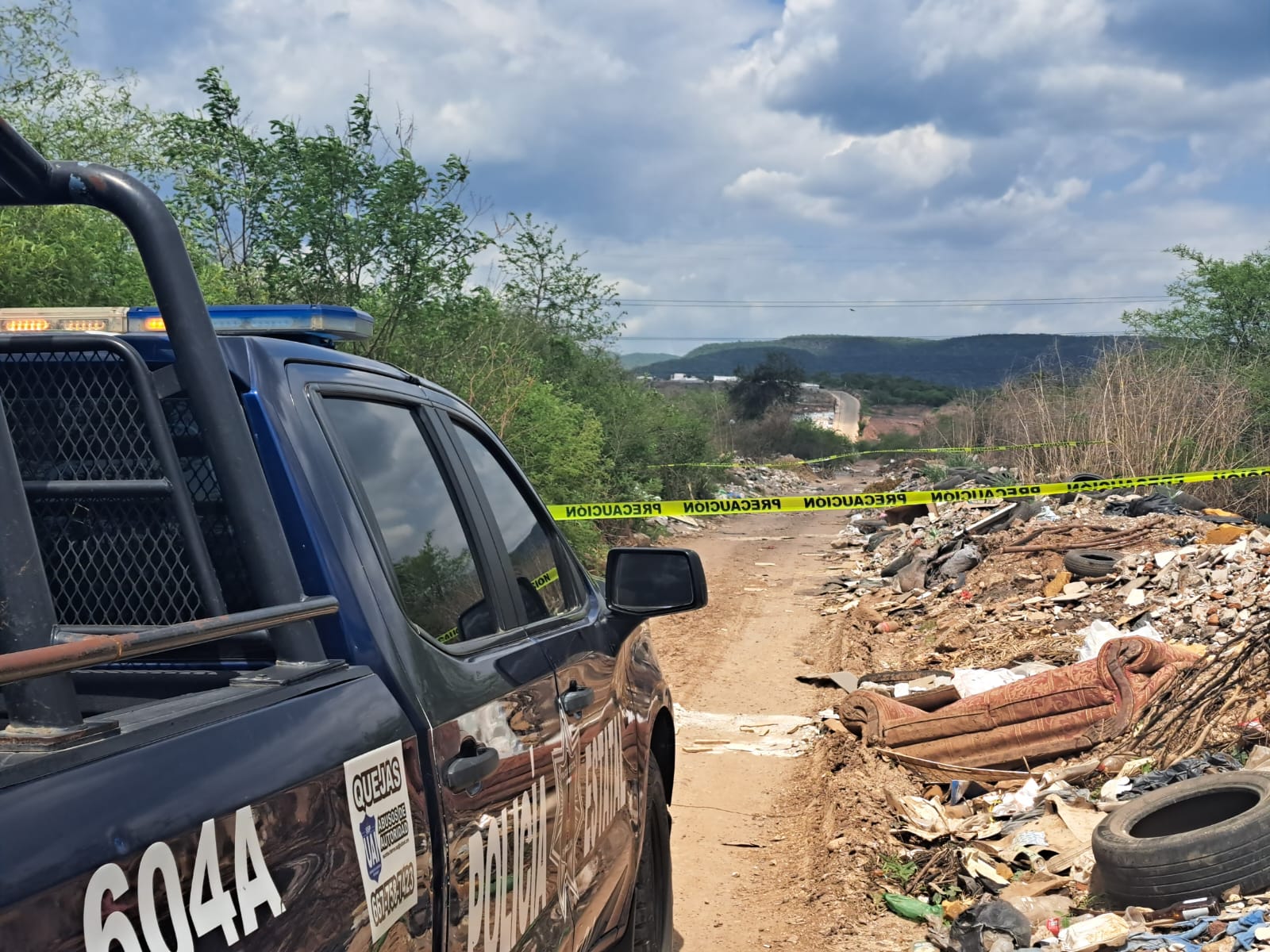 Camioneta de la Policía Municipal de Culiacán, una calle de terracería, árboles y basura