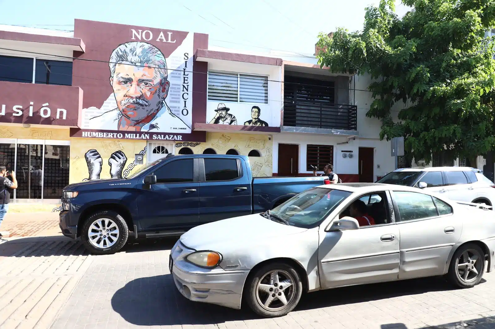 Mural con la imagen de Humberto Millán Salazar y carros pasando por el lugar
