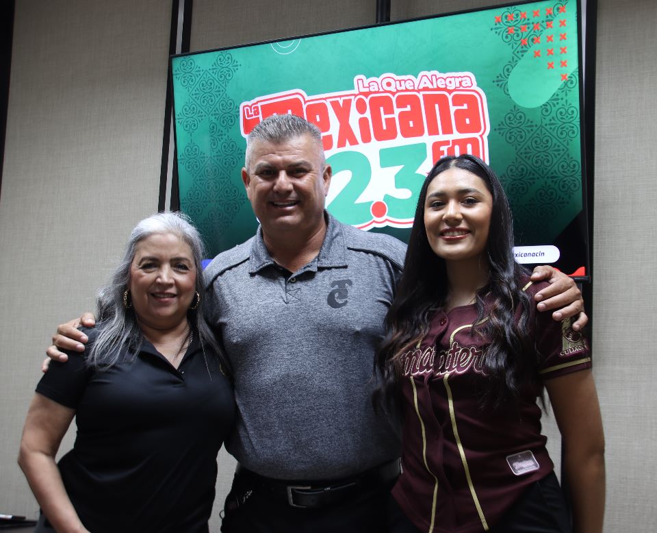 3 personas paradas abrazadas posando para una foto y al fondo una pantalla de tv con letras de una estación de radio