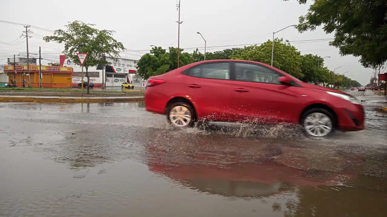 Carro color rojo circulando por calle con agua por lluvias