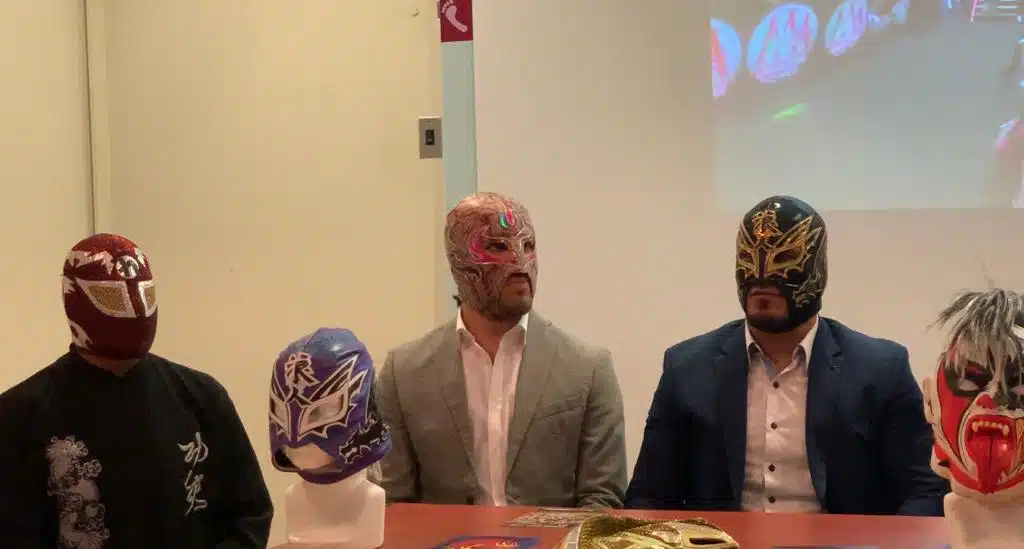 3 personas con máscaras de luchadores sentadas y 2 máscaras más