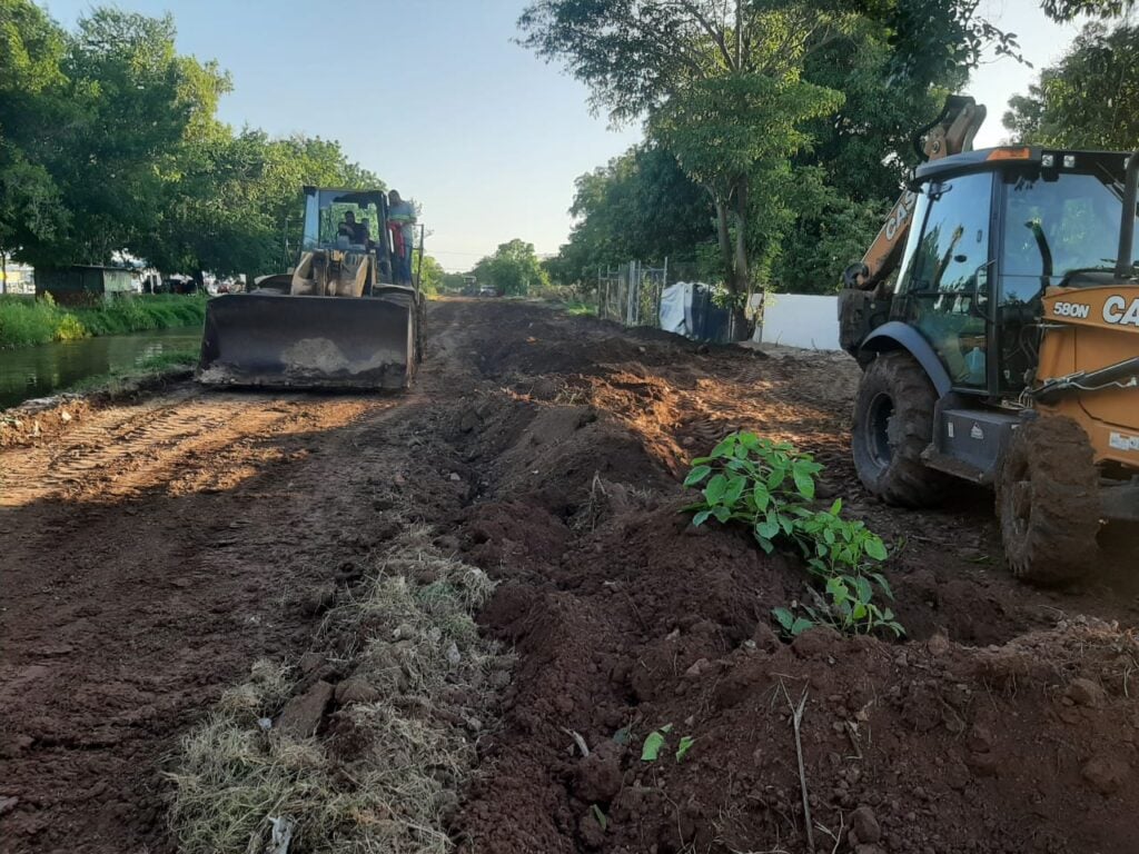 Dos maquinas retroexcavadora rellenando una parte de un canal, árboles al fondo