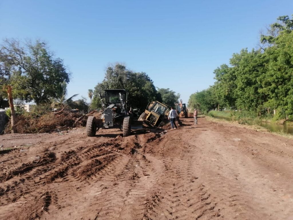 Dos maquinas retroexcavadora rellenando una parte de un canal, árboles al fondo