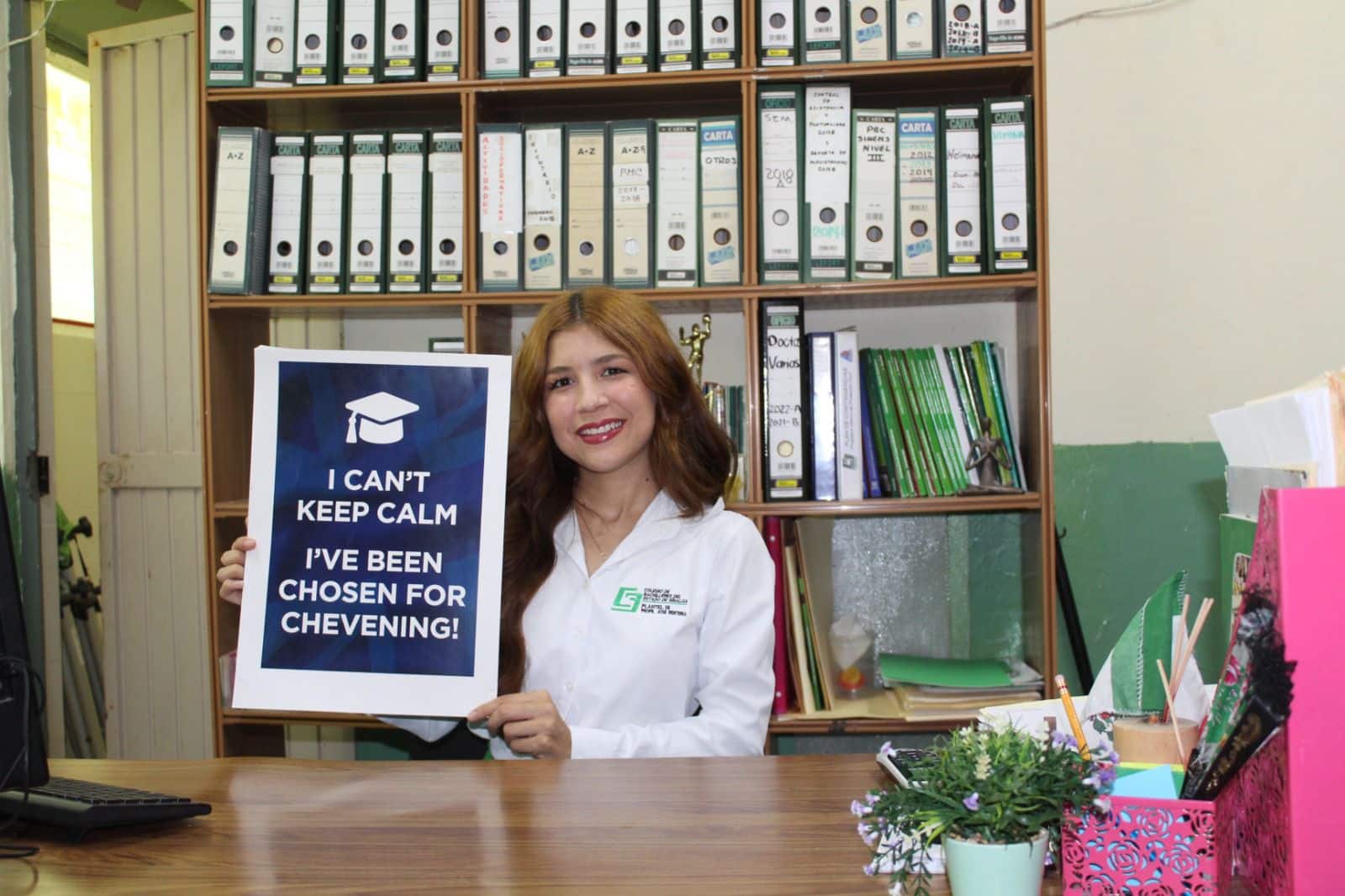 Una persona sentada sonriendo con un cartel en la mano