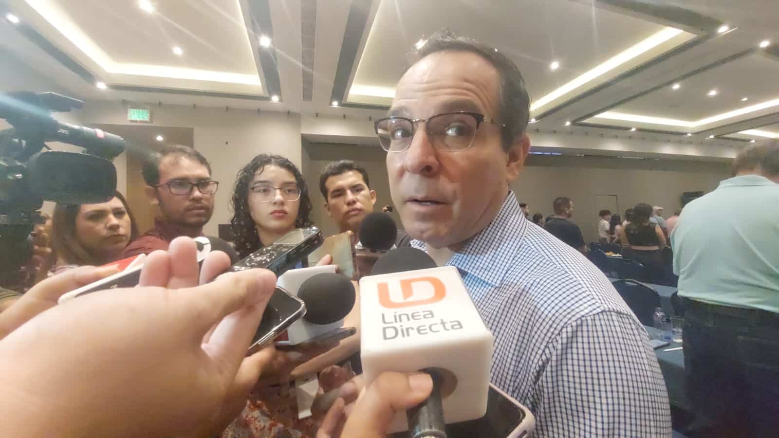 Una persona hablando con los medios de comunicación, micrófonos, más personas y manos