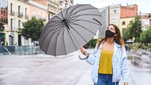 Una persona con saquito, un paraguas, edificios al fondo y una calle mojada