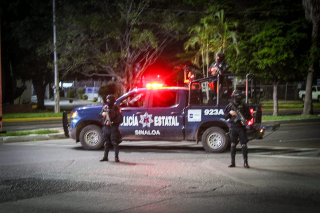 Camioneta de la Policía Estatal y personas encapuchadas paradas