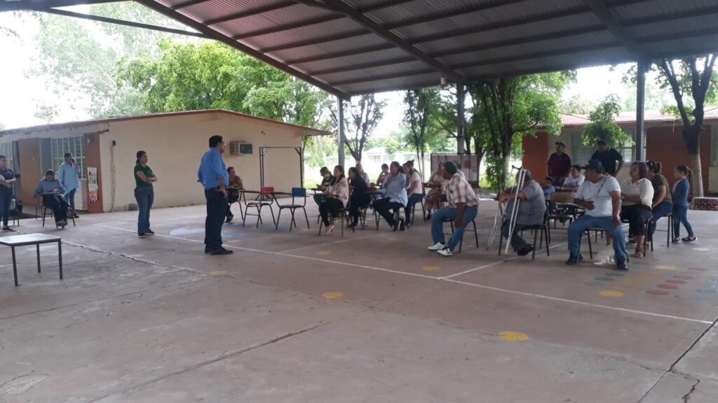 Personas sentadas y otras paradas en la plaza cívica de una escuela