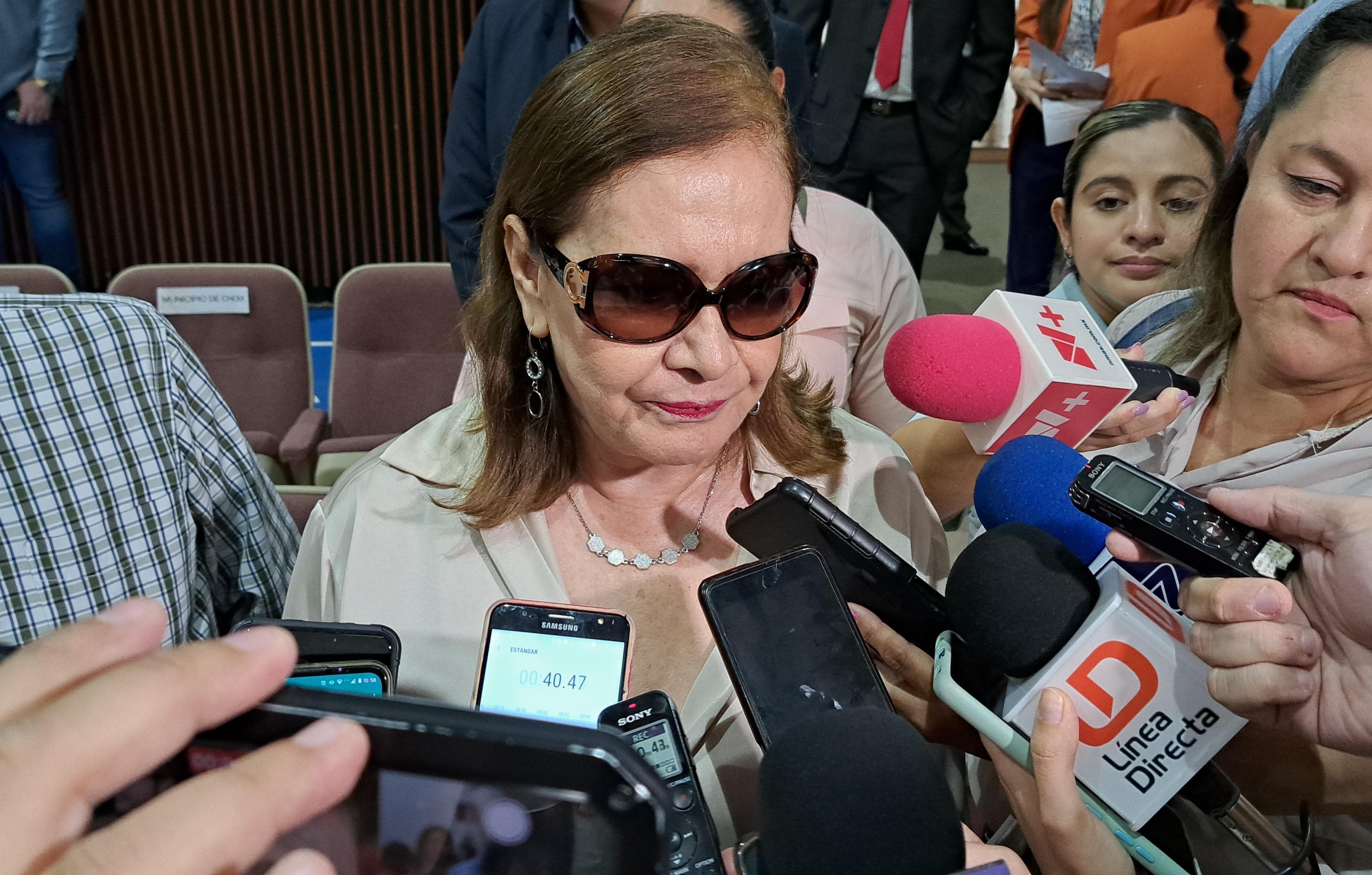 Una mujer con lentes, micrófonos de los medios de comunicación