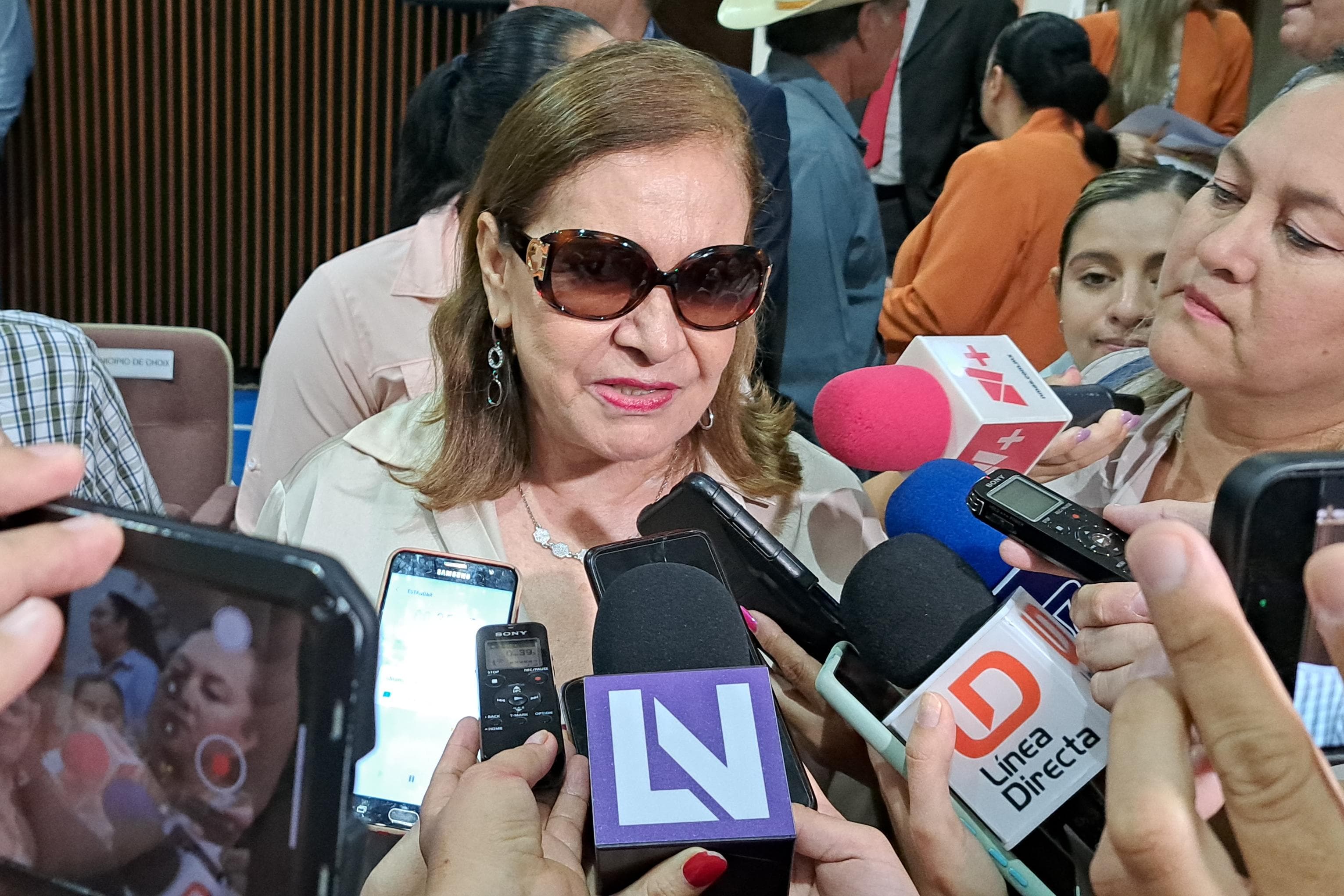 Una mujer con lentes, micrófonos de los medios de comunicación