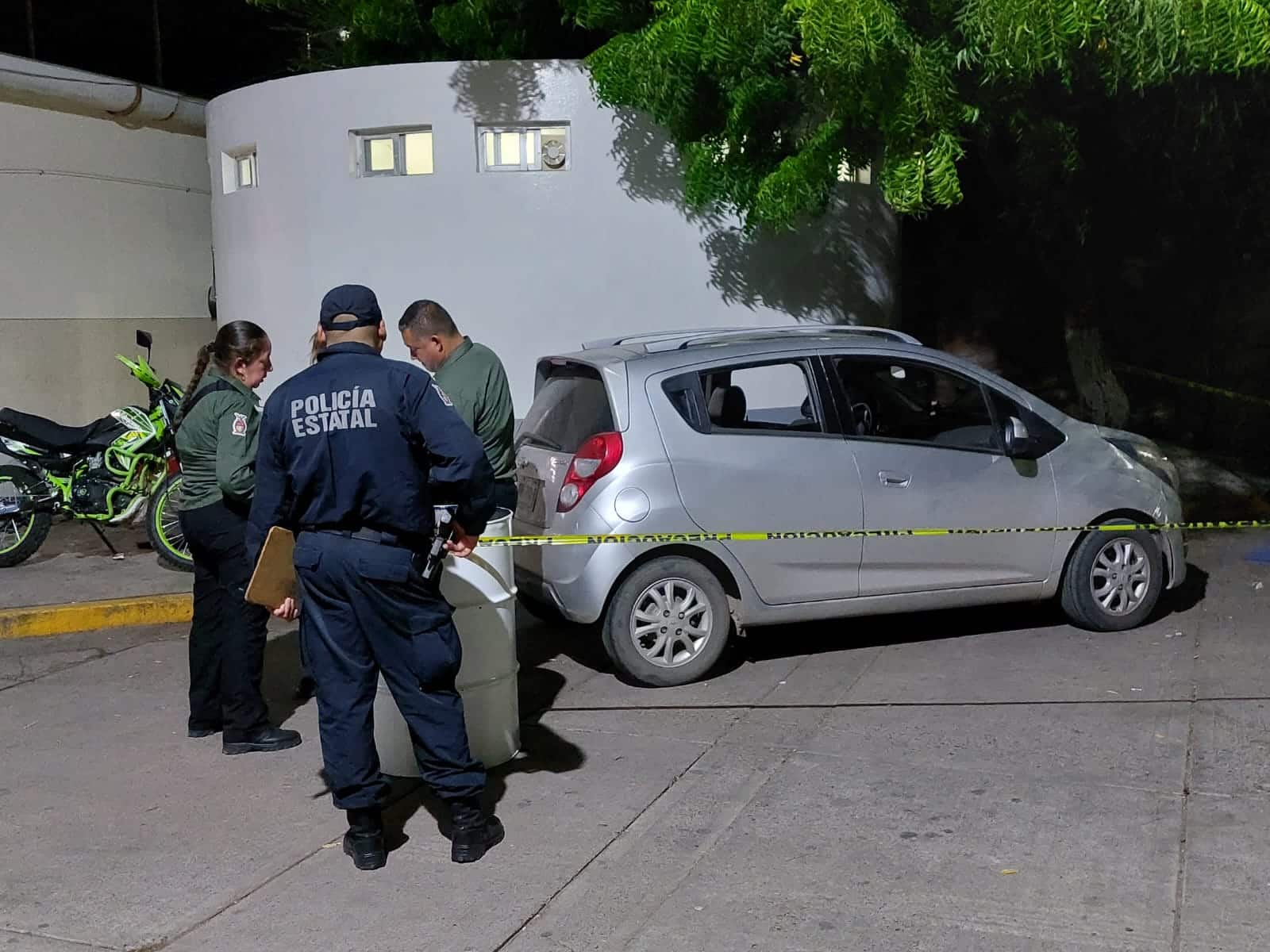 Cinta amarilla delimitando la zona de un crimen, un spark gris y personas mirando hacía él