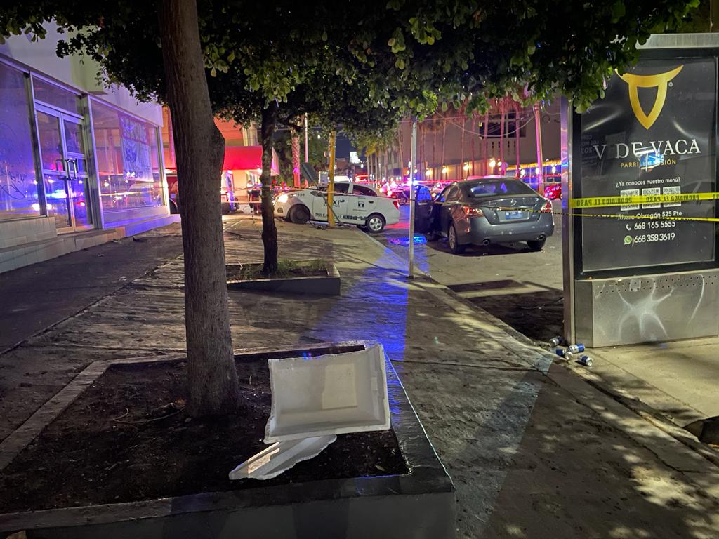 Un taxi chocado, postes, árboles, carros y una cinta amarilla delimitando el área del accidente