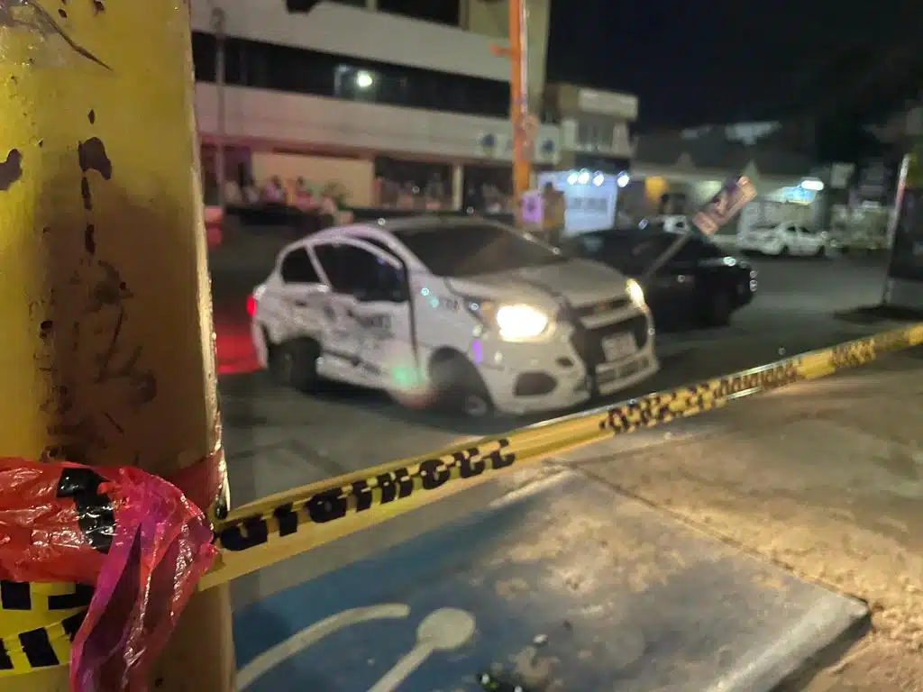 Un taxi chocado, un poste y una cinta amarilla delimitando el área del accidente