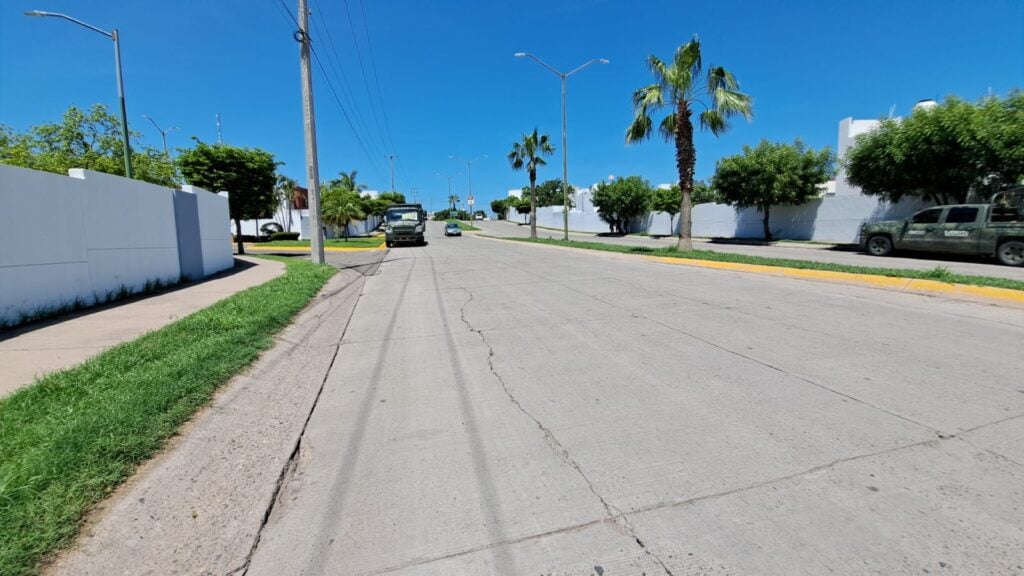 Un camión de los militares estacionado afuera de un privada, camellón, palmeras, árboles, carros, barda de una privada y una camioneta de la Guardia Nacional