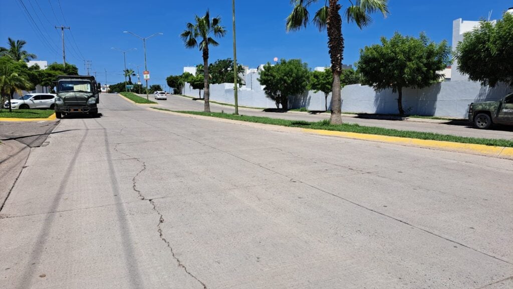 Un camión de los militares estacionado afuera de un privada, camellón, palmeras, árboles, carros y barda de una privada