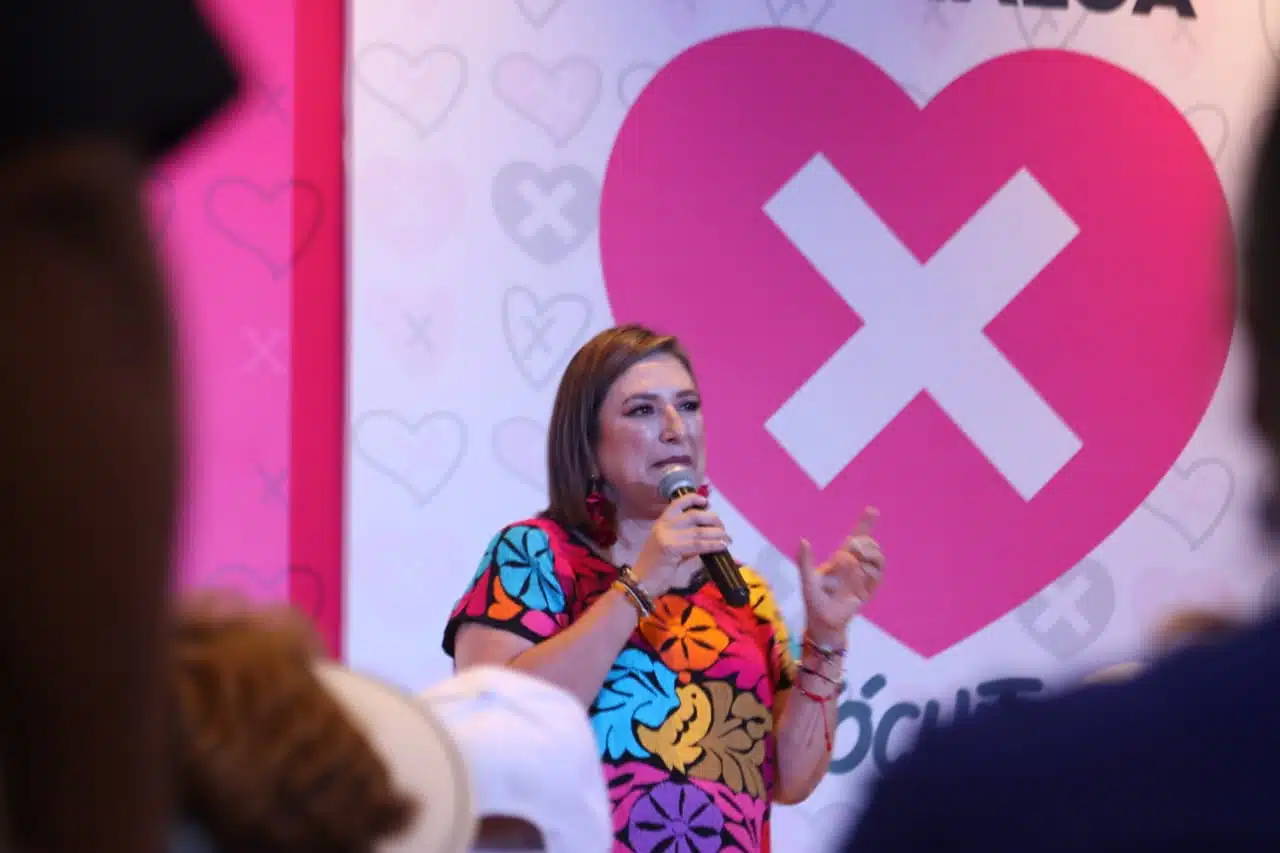Una persona hablando, un micrófono y un corazón con una X al fondo