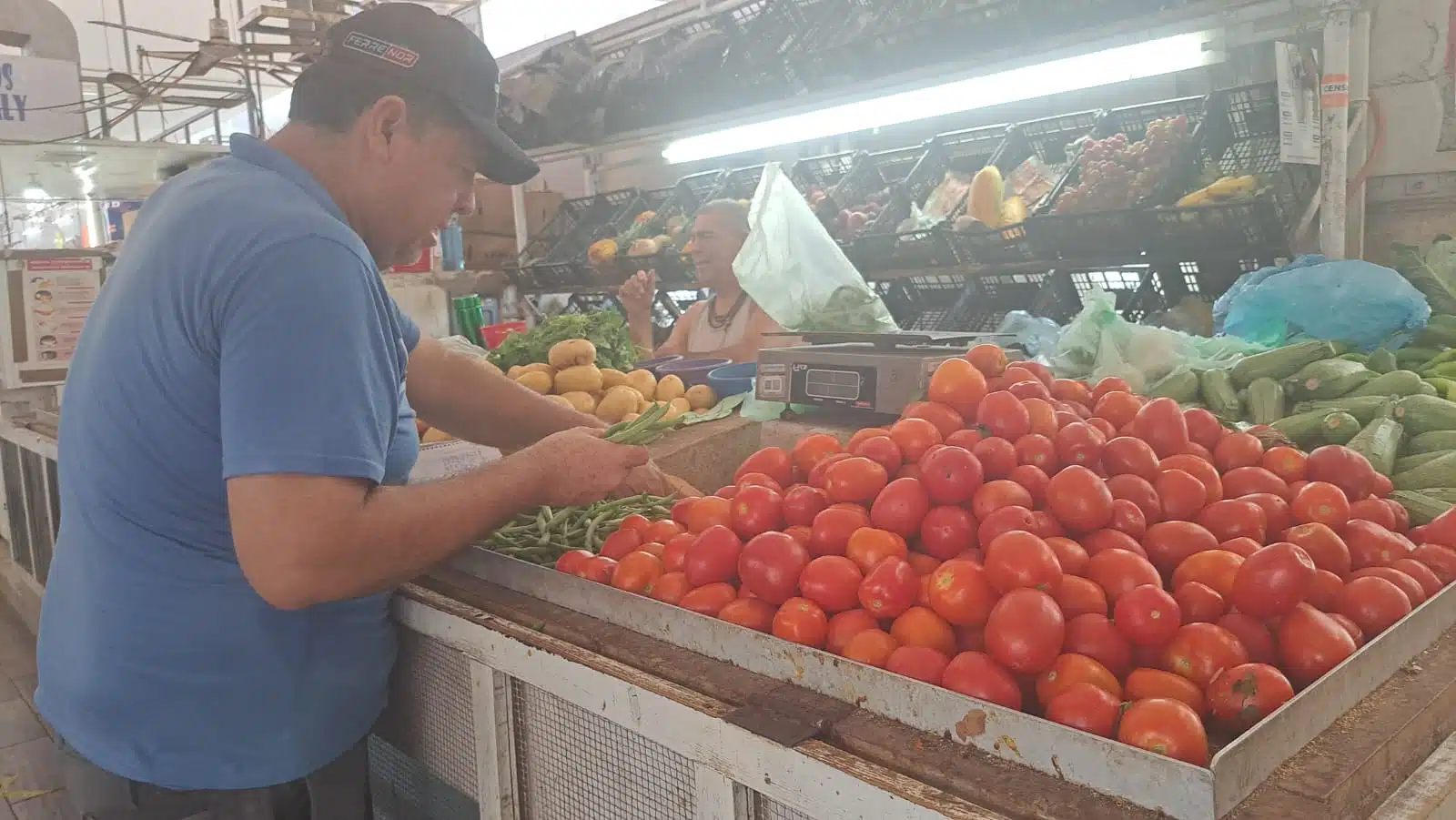 Hombre acomodando ejotes en un puesto de verduras en el mercado