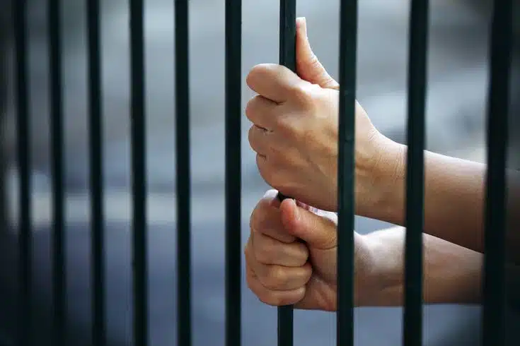 Prisionero en cárcel agarrando barrotes
