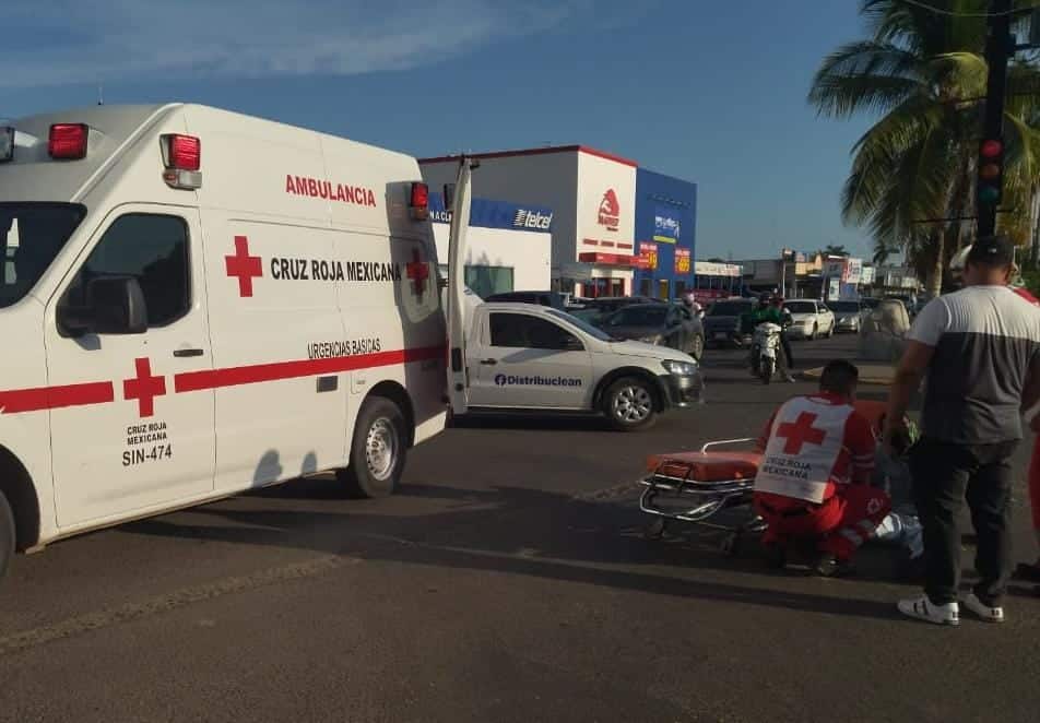 Paramédicos de Cruz Roja atendiendo a una persona en el pavimento. Hay una ambulancia con las puertas abiertas