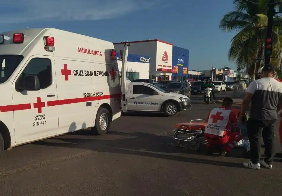 Paramédicos de Cruz Roja atendiendo a una persona en el pavimento. Hay una ambulancia con las puertas abiertas