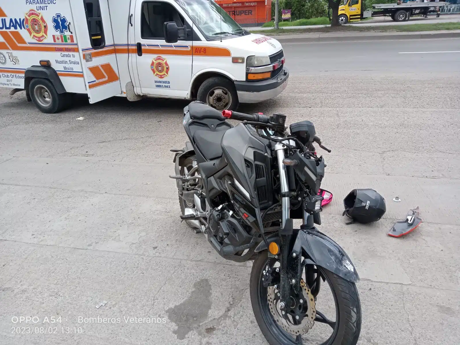 Motocicleta con daños leves por accidente, una ambulancia al fondo y un casco tirado en el pavimento