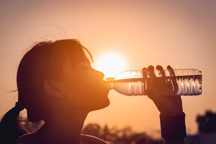 Una persona tomando agua de una botella con el sol de fondo
