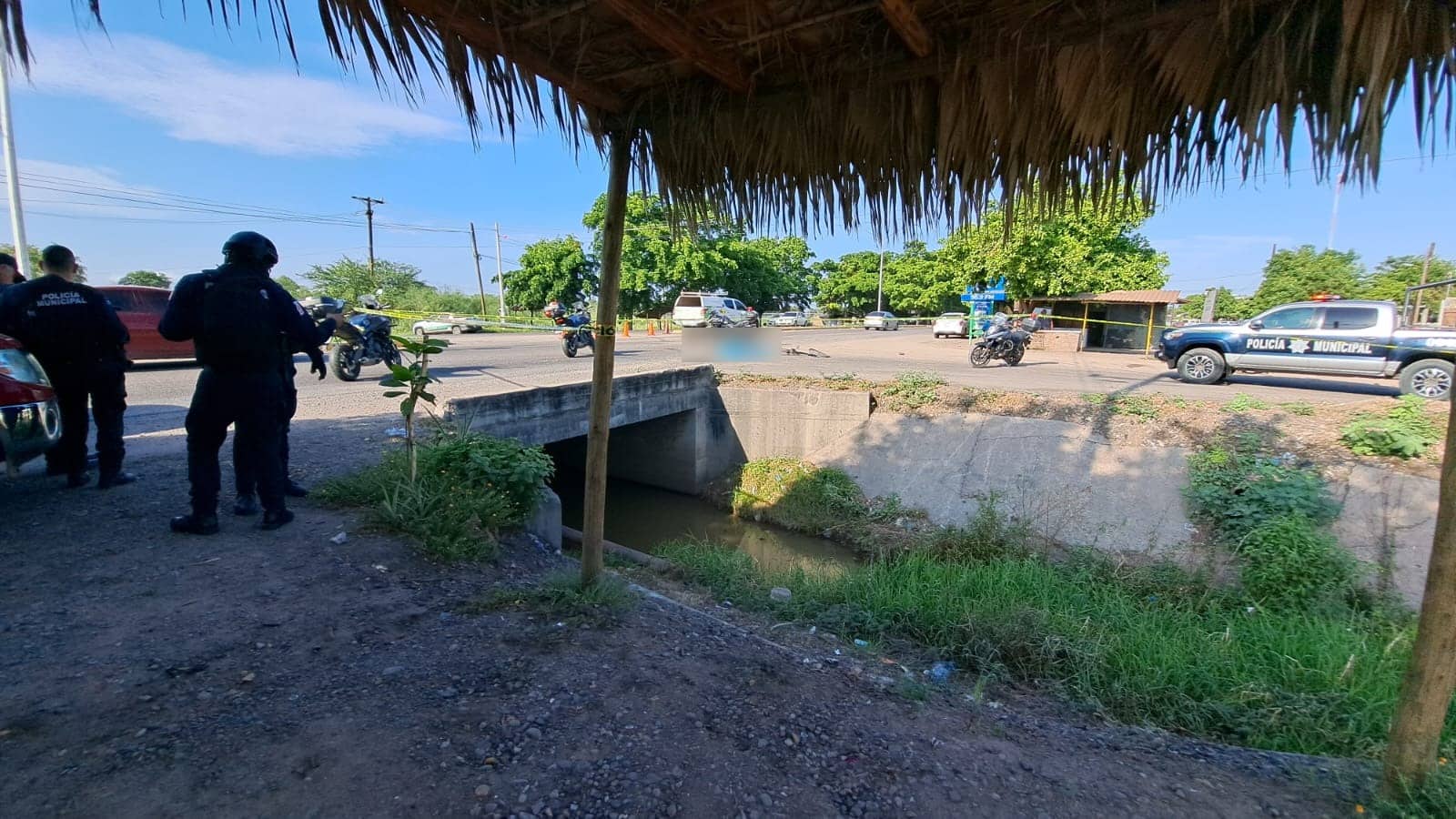 Policía Municipal y Estatal, motocicletas, carros, árboles y carretera, un cuerpo tapado con una tela azul