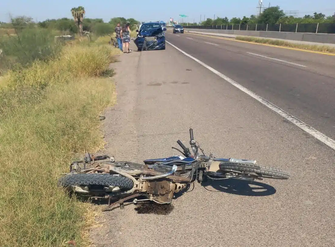 Una motocicleta tirada sobre el pavimento, una carretera, ramas y una camioneta chocada de la parte del frente