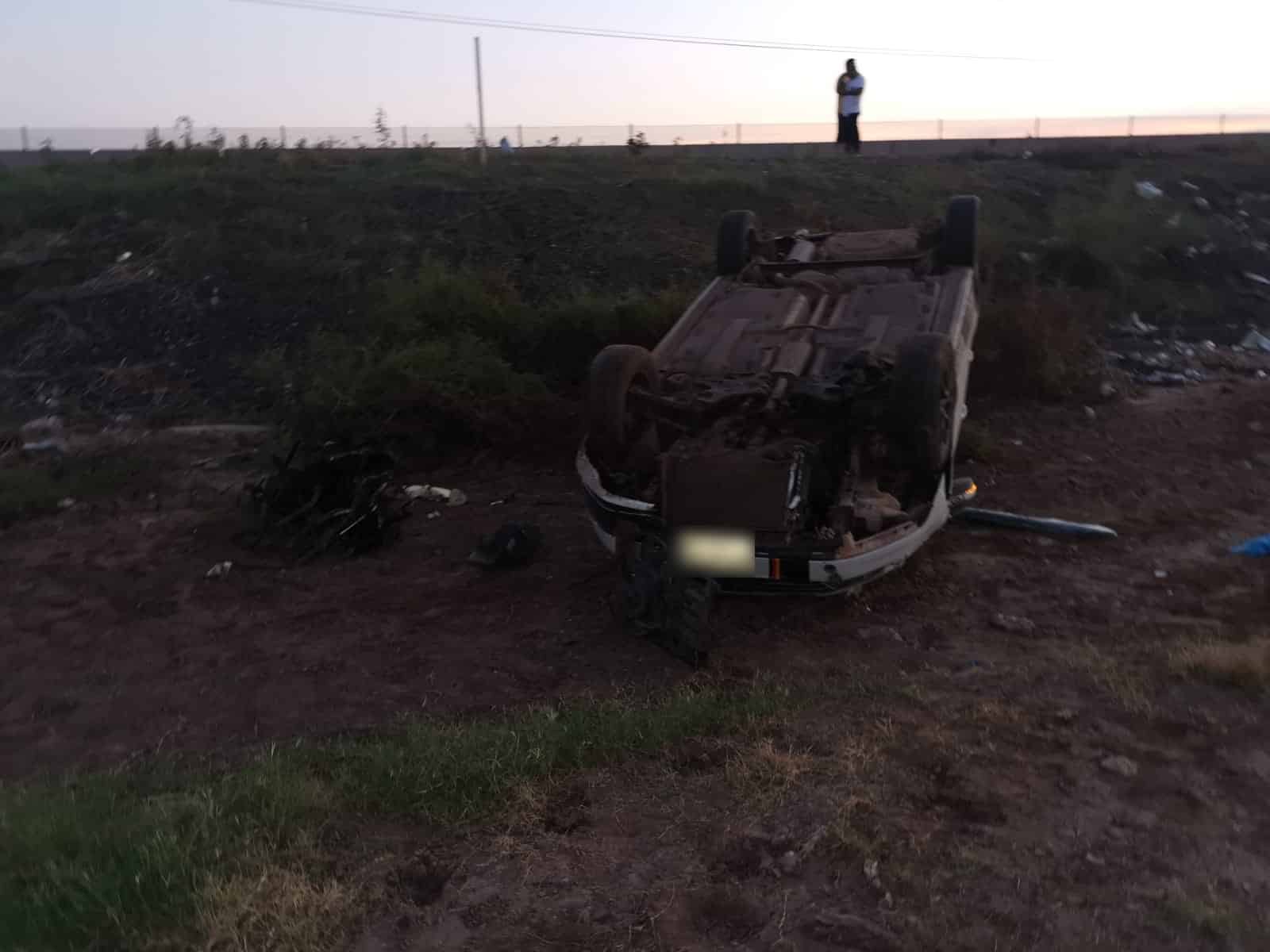 Un carro con le neumáticos hacia arriba a un lado de la carretera y una persona mirando