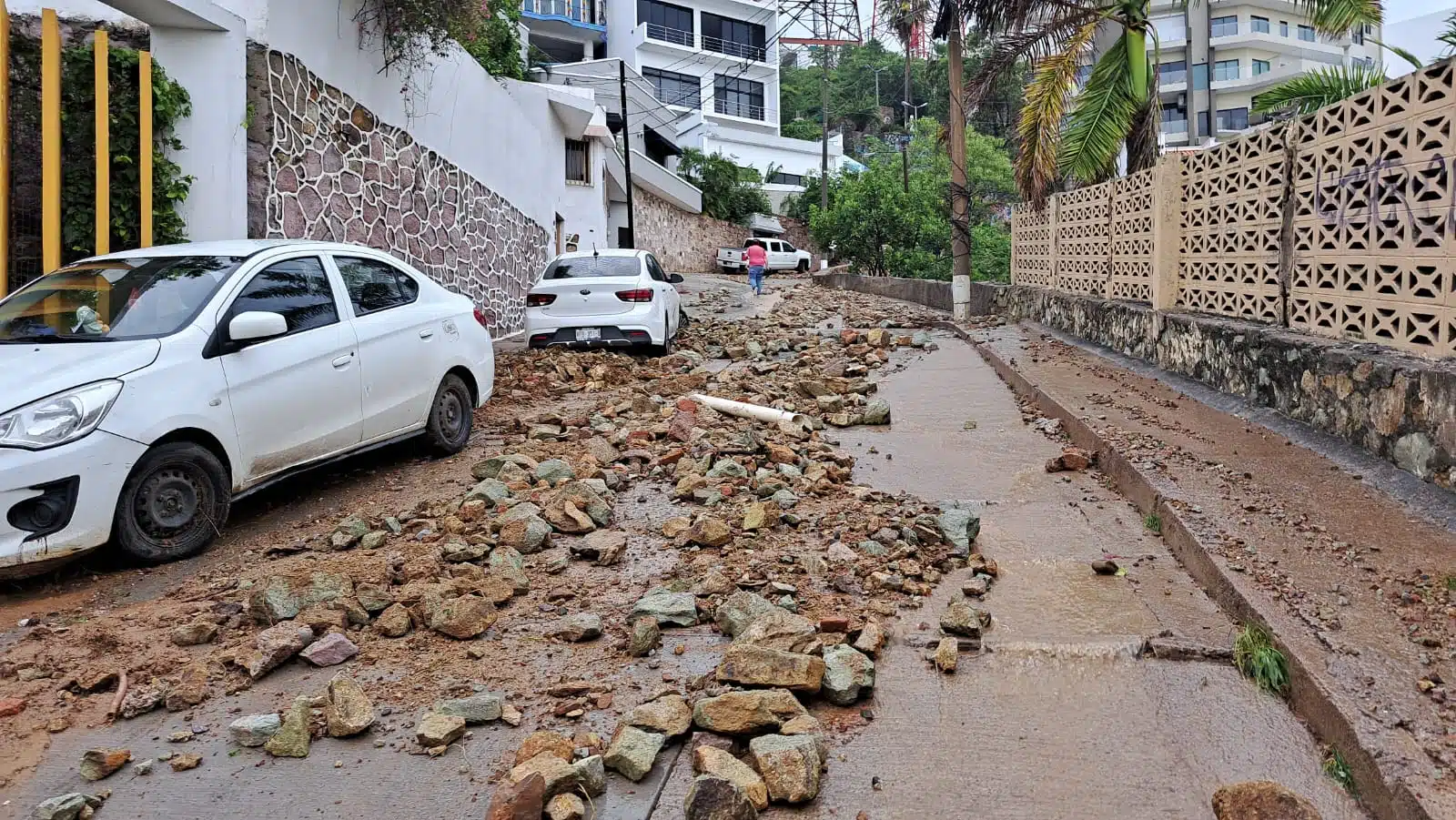 Piedras y tierra sobre una calle, carros estacionados y casas