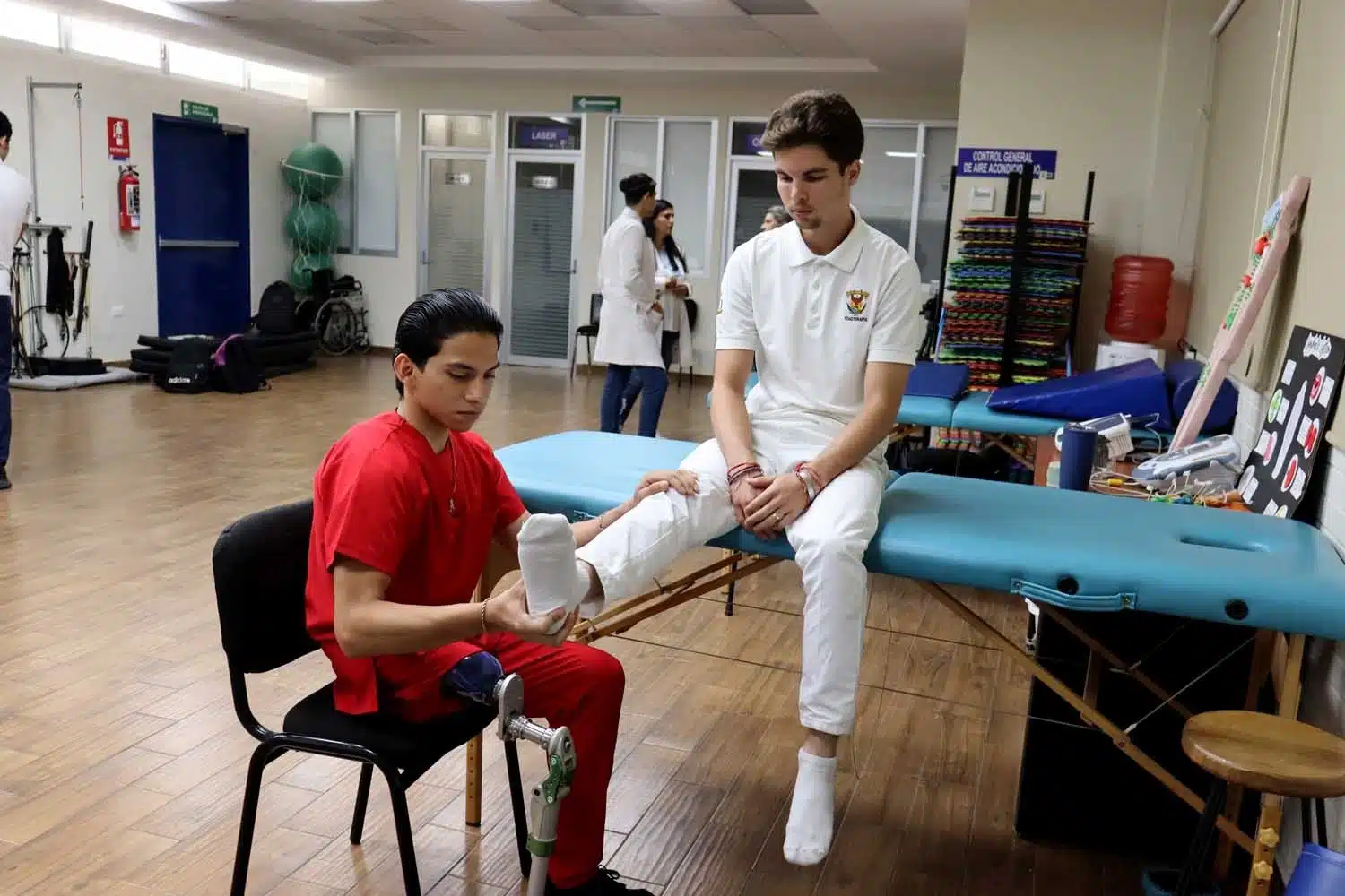 Una persona sentada con una prótesis de pierna dando terapia a otra