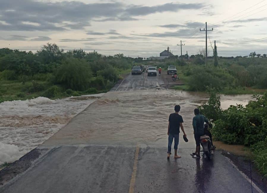 2 personas mirando a un arroyo desbordándose y pasando sobre la carretera