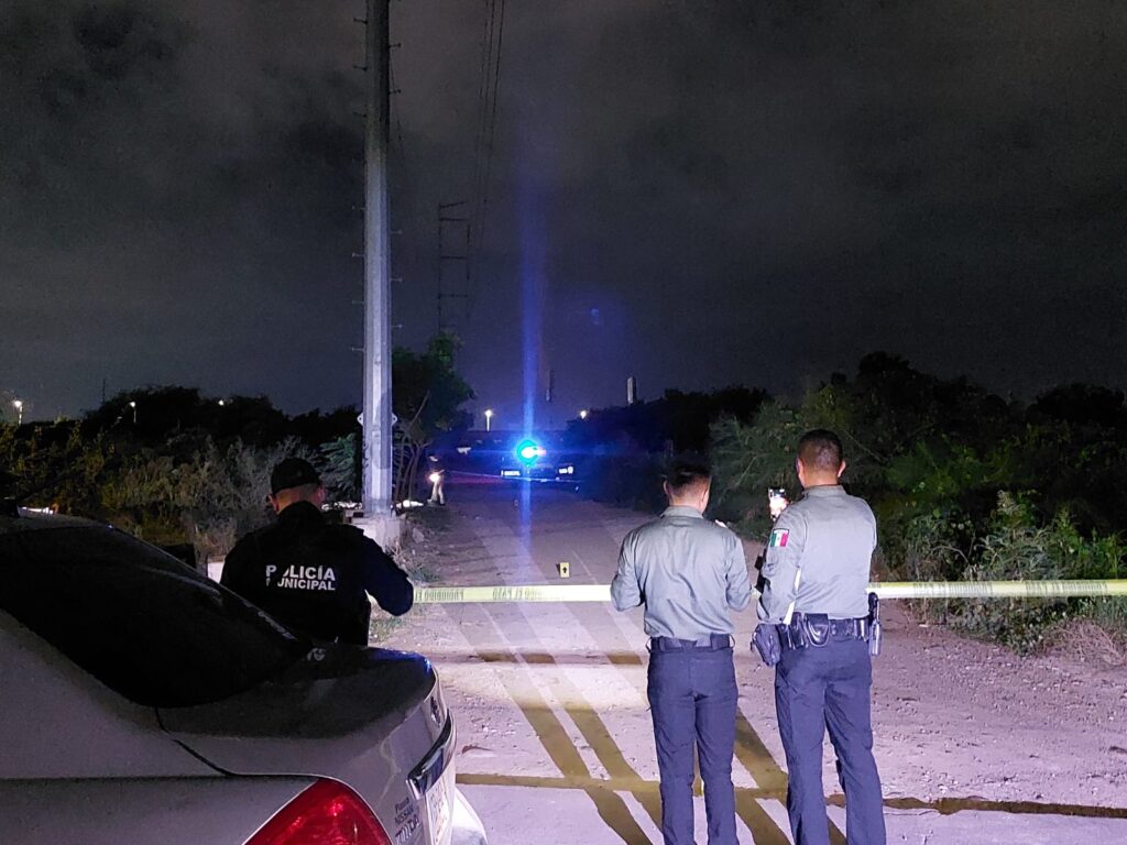 Personas mirando hacia donde fue un crimen, cinta amarilla delimitando el área y carros