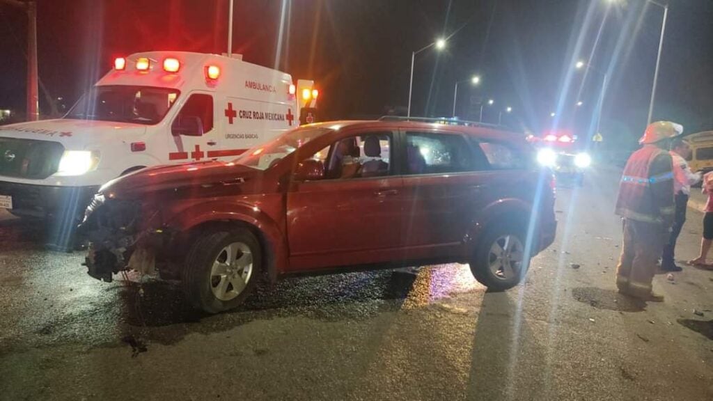 Camioneta chocada en medio de calle y una ambulancia a un lado en la obscuridad