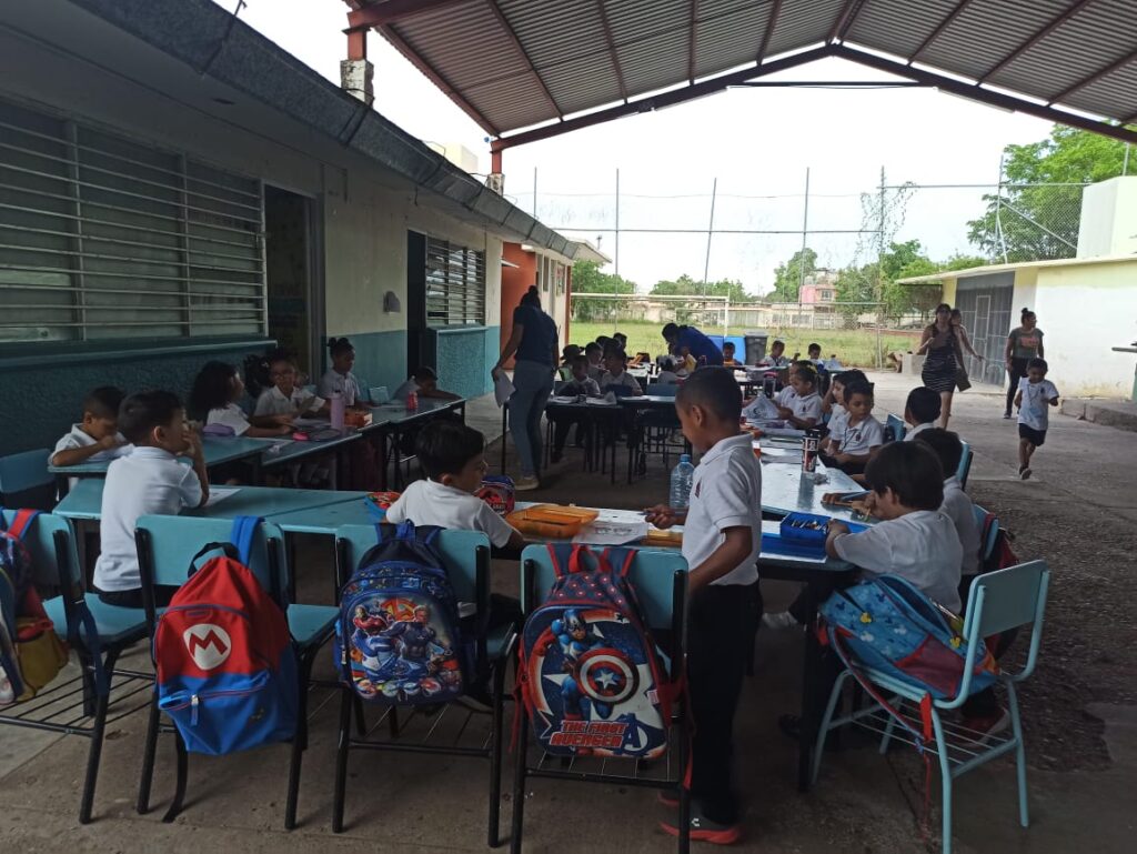 Niños sentados tomando clases fuera del aula