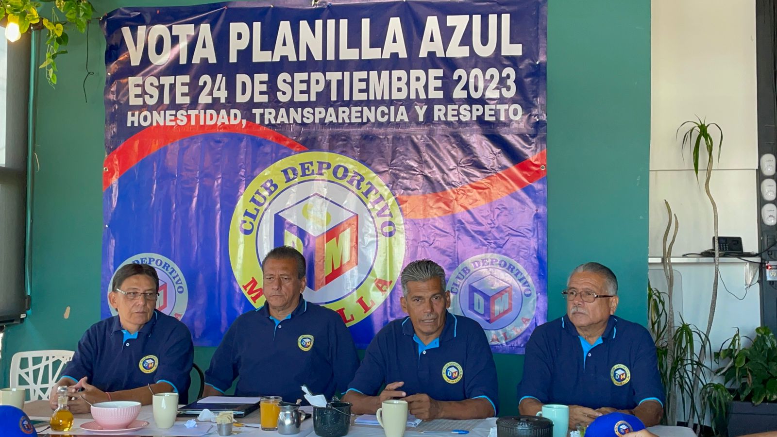 4 personas sentadas en una conferencia de prensa al fondo una lona