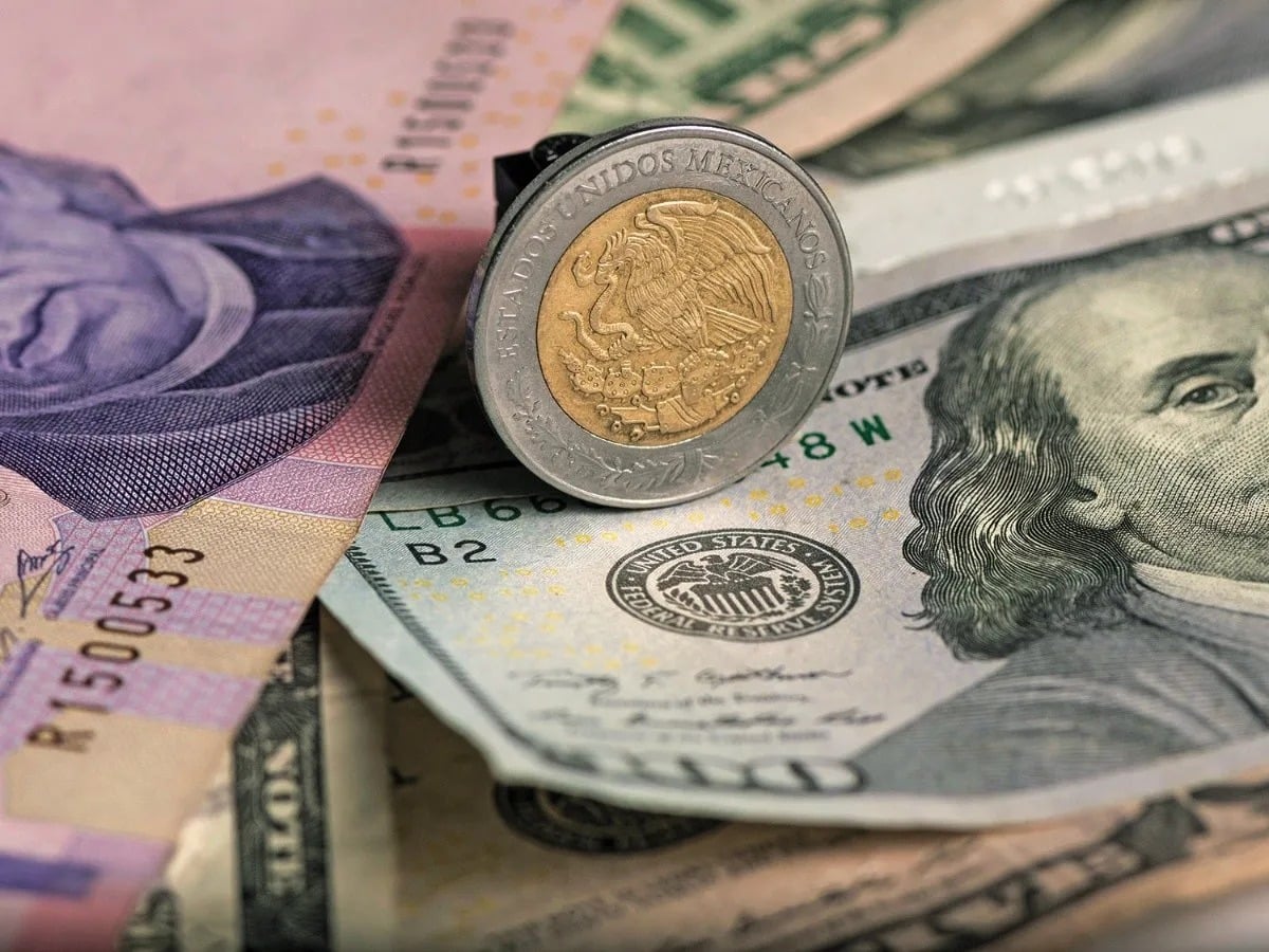 Billete de 100 dólares junto a una moneda de 1 peso