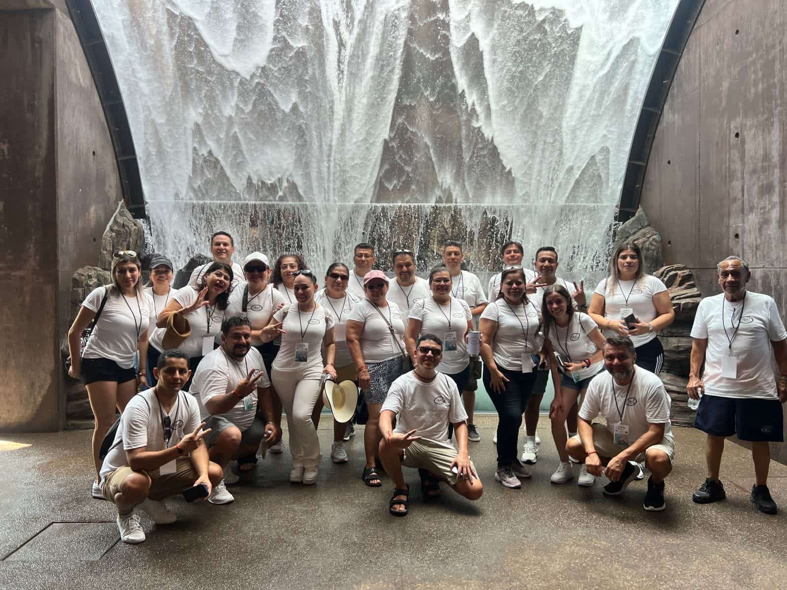 Personas posando para una foto y agua cayendo en forma de cascada al fondo